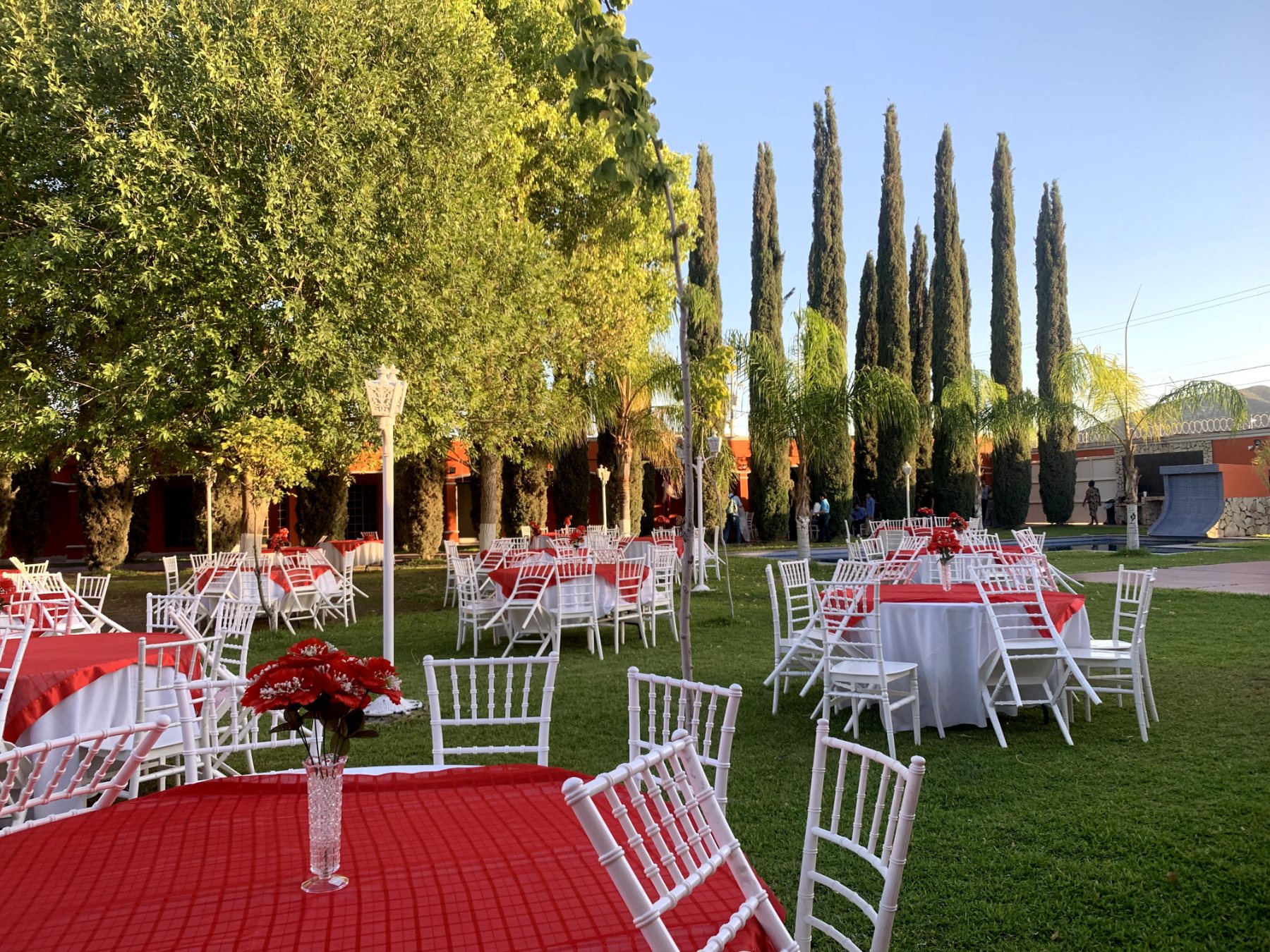 Jardín de Quinta Paris con mesas redondas cubiertas con manteles rojos y sillas blancas, adornadas con flores rojas, listas para una fiesta de XV años en Lerdo.